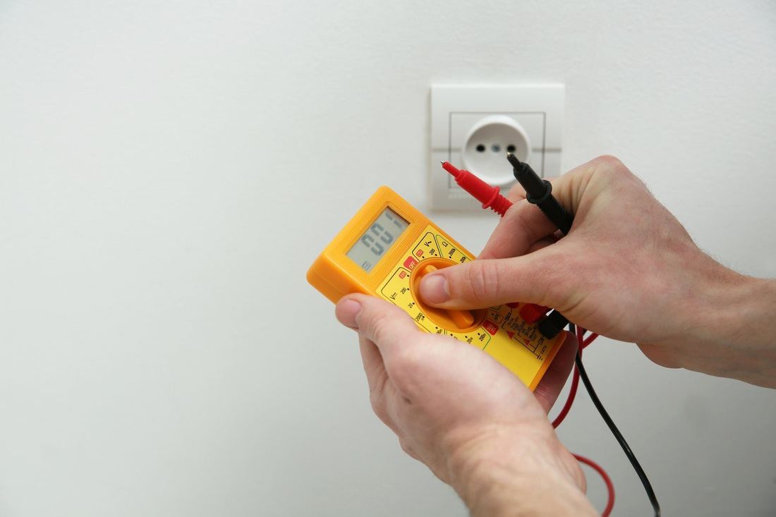 Dłonie elektryka z miernikiem przy starym gniazdku